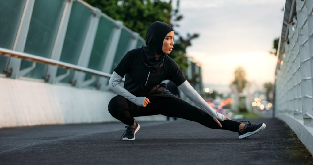 Woman wearing a hijab doing stretches on walkway bridge in the early morning.