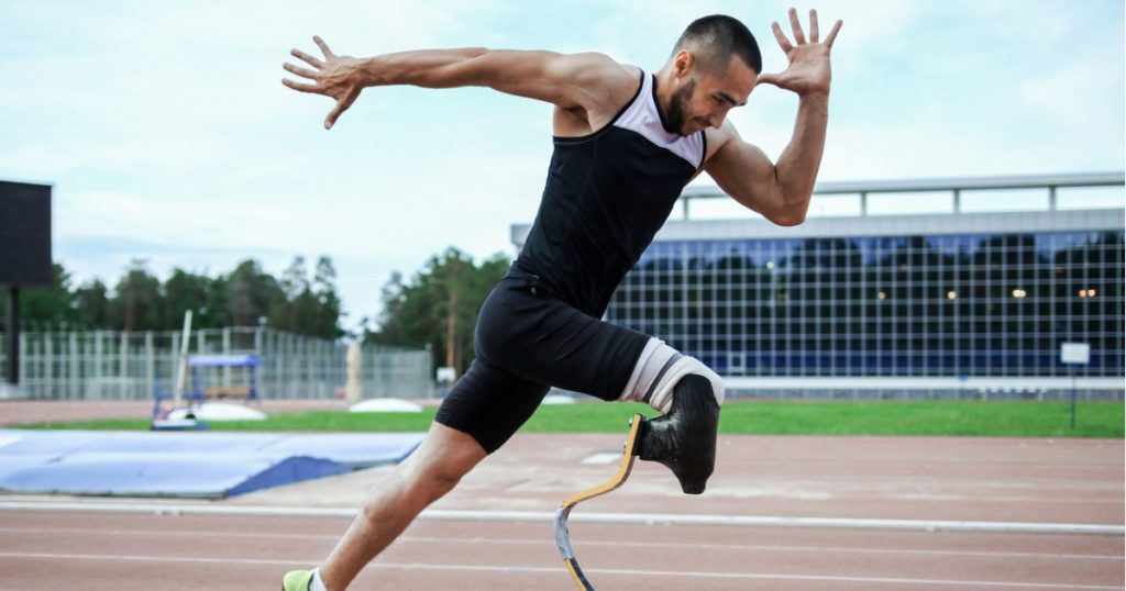 Male athlete with a prosthetic leg in an explosive running position on an outdoor running track.